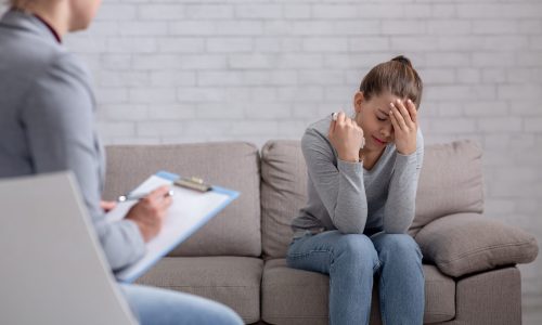Psychological help concept. Millennial woman with depression having counseling session with therapist at office. Desperate young lady with mental illness receiving help from psychiatrist at clinic